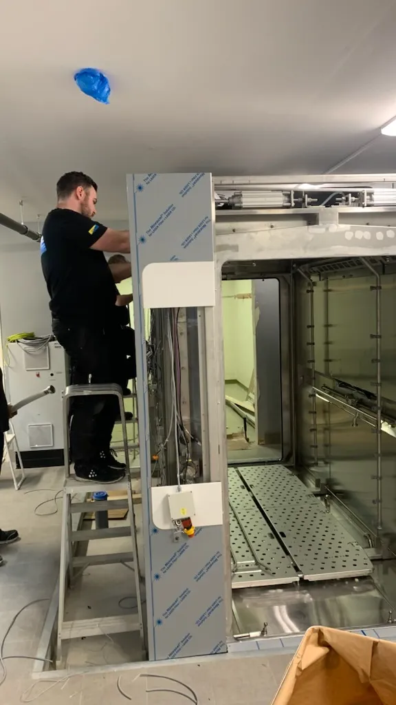 Tekniker som justerar dörrmekaniken på en stor sterilisatorkammare med skyddsfilm kvar