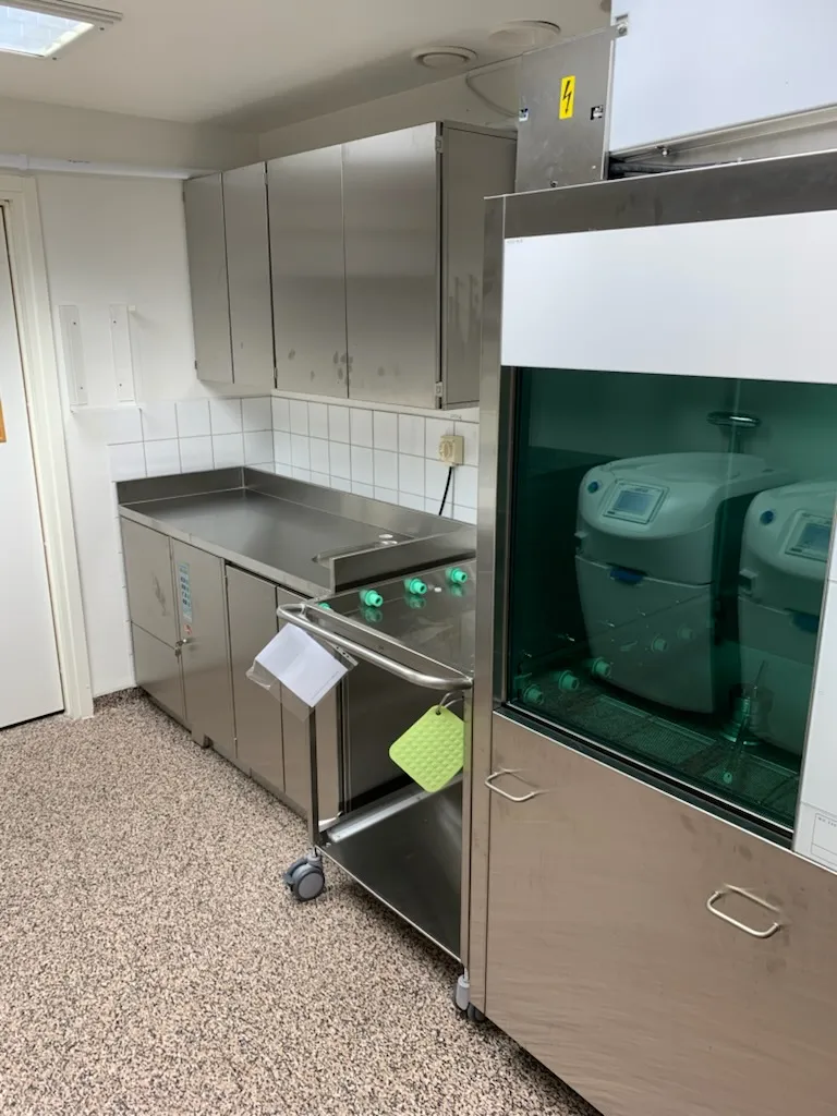 Diskdesinfektor med grön glaslucka och lastvagn intill en rostfri bänk i en sterilcentral