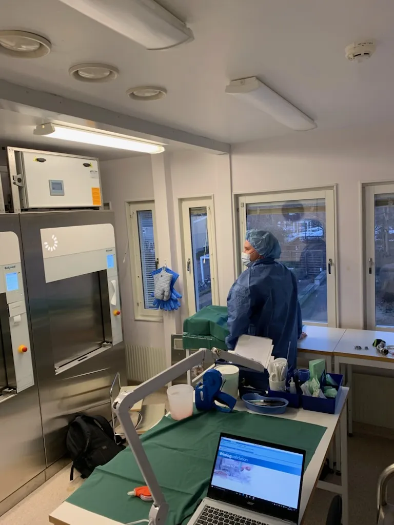 Personal i skyddsdräkt framför en autoklav i drift med mätdator uppkopplad på bänken