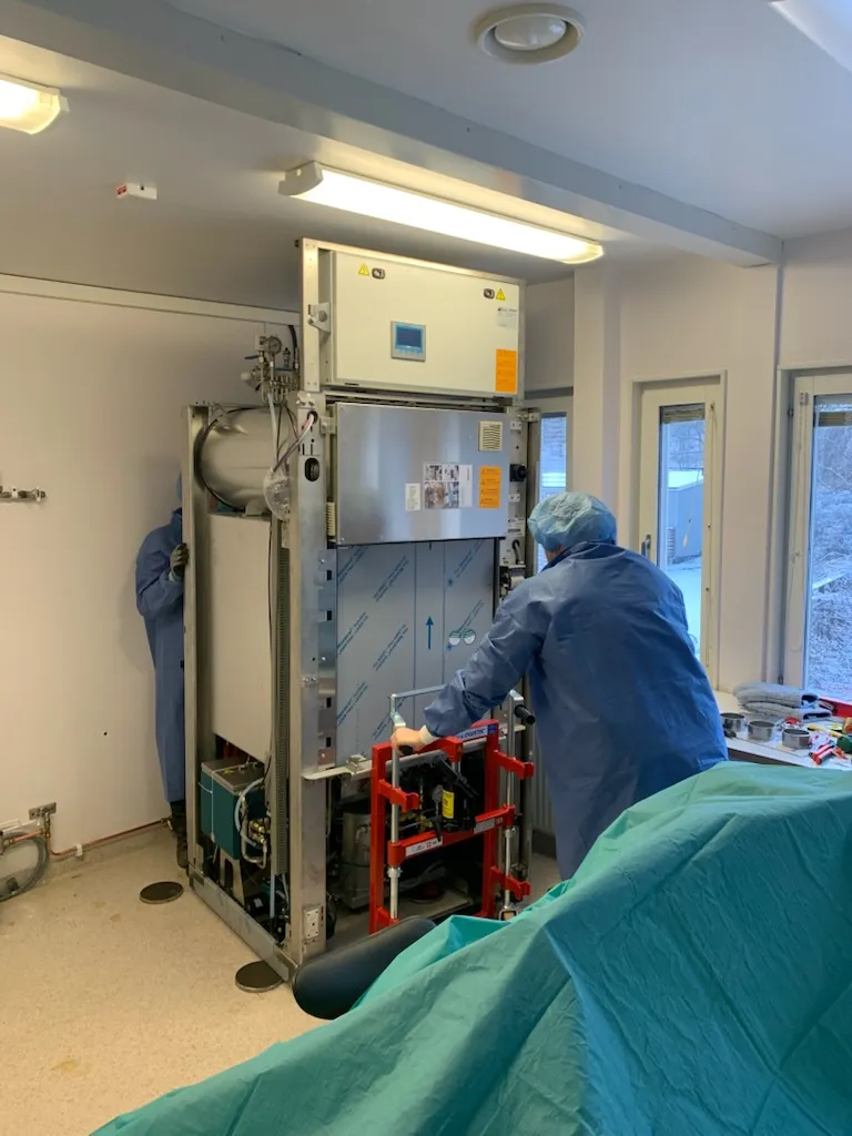 Tekniker i skyddsdräkt som monterar en stor autoklav på pallyft i ett behandlingsrum